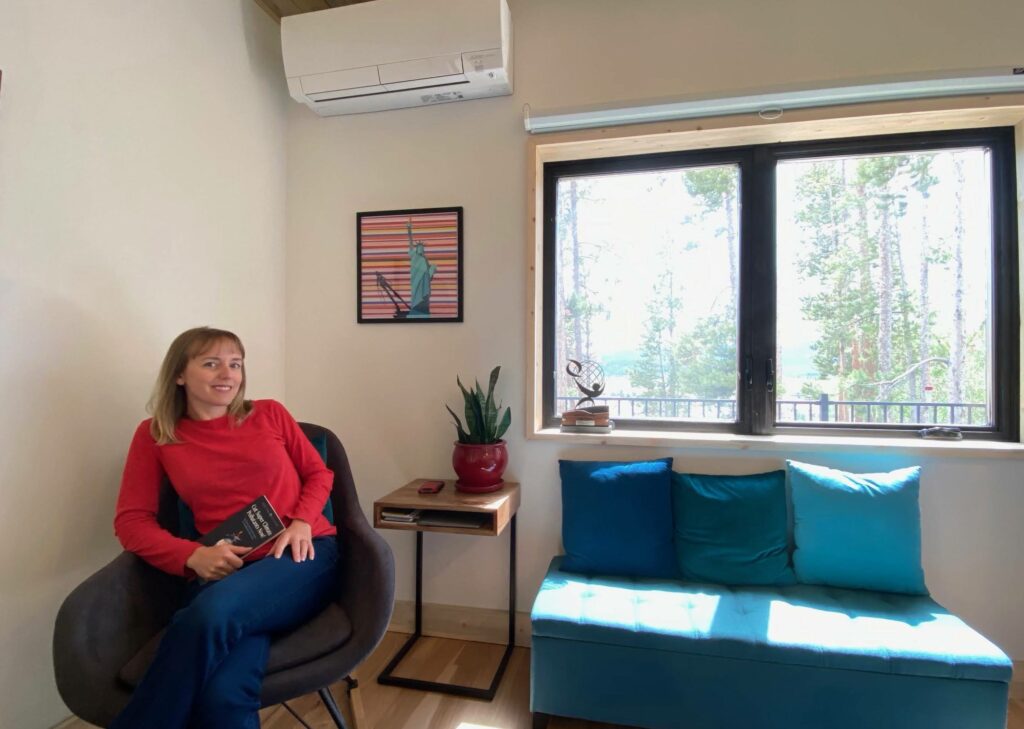 Kristen Taddonio sits in her new home, which took first place in the U.S. Department of Energy Solar Decathlon Build Challenge as the entry from the University of Colorado Boulder. One of the "mini-splits' of the heat pump system that warms and cools the house is on the wall above her head. Photo Courtesy of Kristen Taddonio