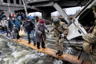 Residents of Irpin flee heavy fighting via a destroyed bridge as Russian forces entered the city on March 7, 2022 in Irpin, Ukraine. Credit: Chris McGrath/Getty Images