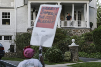 A resident watches as abortion-rights advocates stage a protest near the home of U.S. Supreme Court Chief Justice John Roberts on May 11, 2022 in Chevy Chase, Maryland. Credit: Kevin Dietsch/Getty Images
