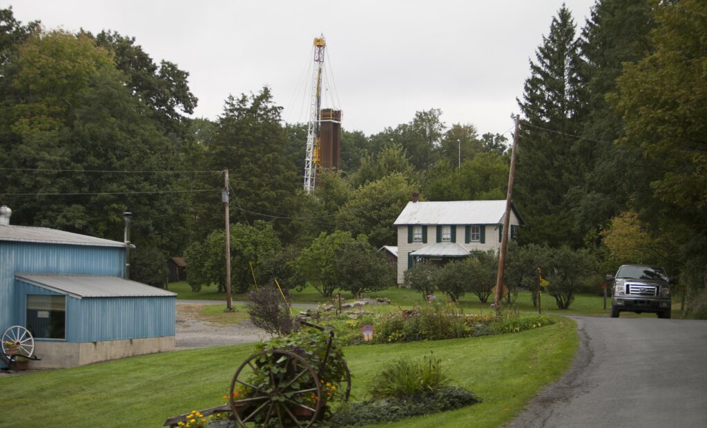 A car drives by a home with a nearby derrick drilling for natural gas near Calvert, Pennsylvania. Credit: Robert Nickelsberg/Getty Images.