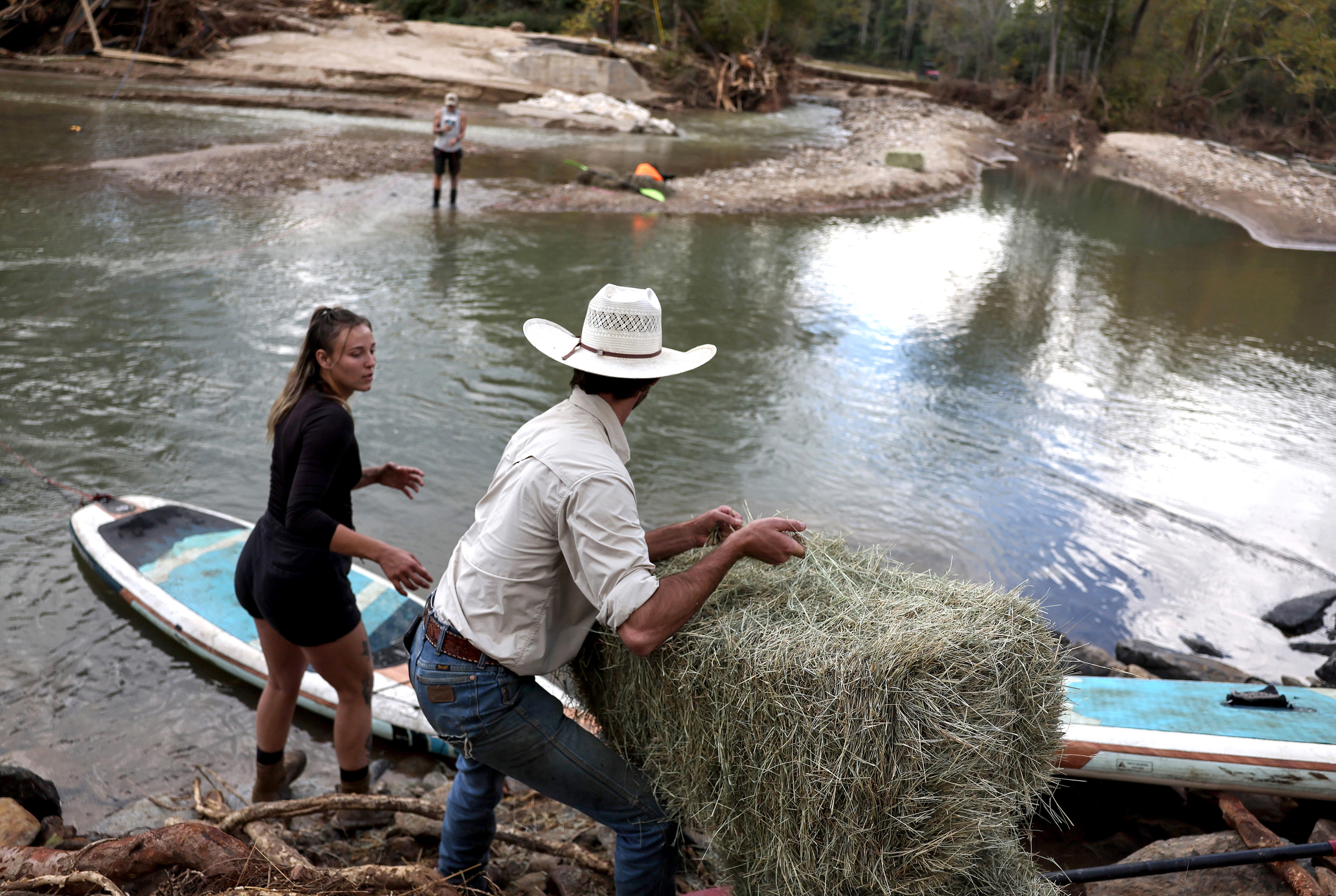 Hudson Johnson passes hay to Kristen Kiker, as she prepares to tow it across floodwaters with a paddleboard to feed horses and goats on a nearby farm in Black Mountain, N.C., on Thursday in the aftermath of Hurricane Helene. Credit: Mario Tama/Getty Images