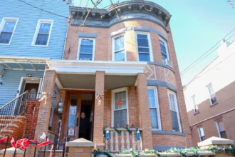 Marisol Genao is smiling in her doorway of a brick end-unit rowhouse