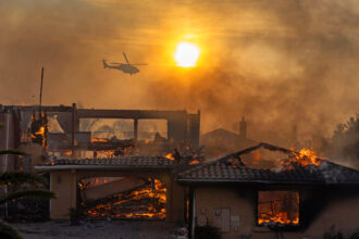A firefighting helicopter flies near as a home burns from the Mountain Fire on Nov. 6 in Camarillo, Calif. Researchers have found areas exposed to high wildfire hazard will double between 2020 and 2070. Credit: David McNew/Getty Images
