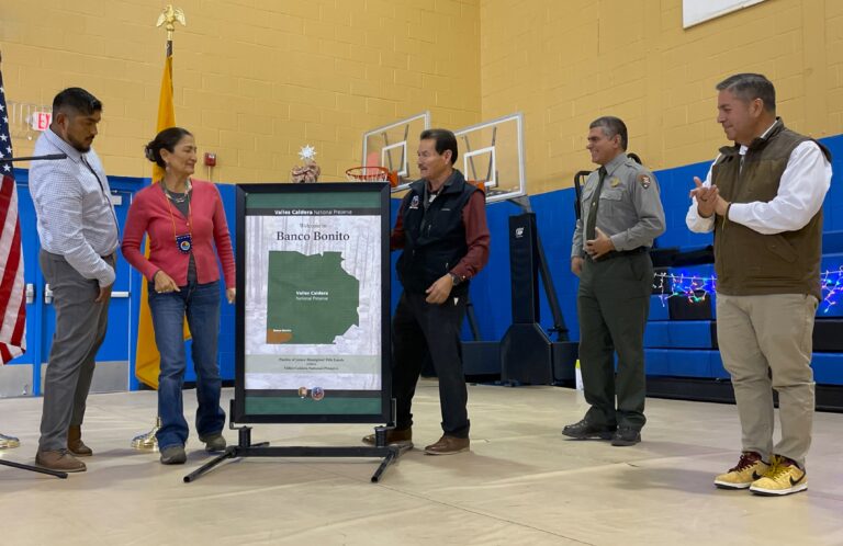 Secretary of the Interior Deb Haaland, second from the left, helped Pueblo of Jemez Gov. Peter Madalena, center, unveil a poster showing Valles Caldera National Preserve in north central New Mexico, during the event on December 22 celebrating the settlement upholding the pueblo’s entitlement to its ancestral land, including Banco Bonito, inside the national preserve. Credit: Noel Lyn Smith/Inside Climate News