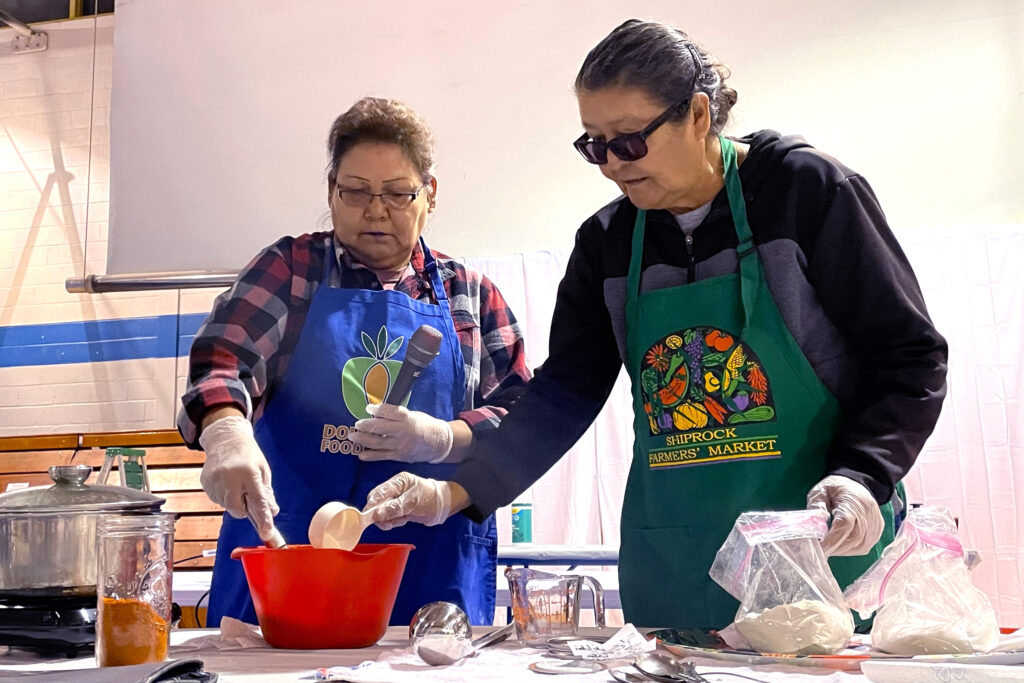 Lorraine Jim (left) and Daryl King prepare chiiłchin, a pudding made from crushed sumac berries, on Nov. 25 at the food gathering summit in Shiprock, N.M. Credit: Noel Lyn Smith/Inside Climate News
