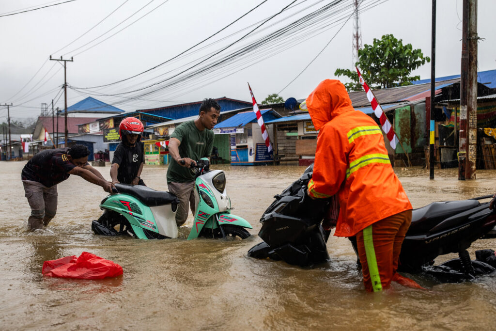 Residents try to move their motorbikes through floodwaters in the Lukulamo Village on Aug. 13, 2024.