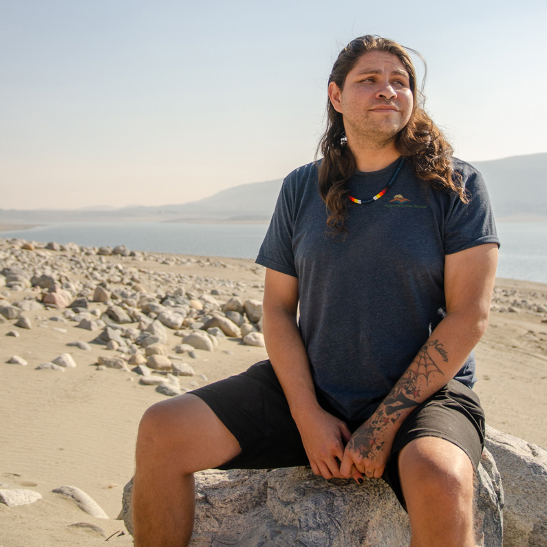 Big Wind Carpenter, a member of the Northern Arapaho tribe, sits on the beach at Bull Lake, a place where Big Wind’s family would recreate decades ago. Credit: Jake Bolster/Inside Climate News