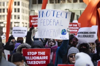 The workers are holding signs with messages like, "Protect federal workers!" and "Stop the Billionaire Takeover"