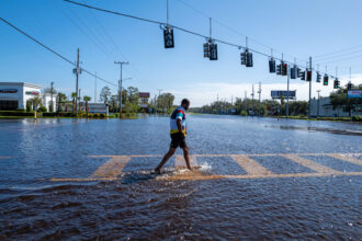 A person walks through a flooded street from the rising Anclote River as the region tries to recover from Hurricane Milton on Oct. 11, 2024, in New Port Richey, Fla. Credit: Spencer Platt/Getty Images