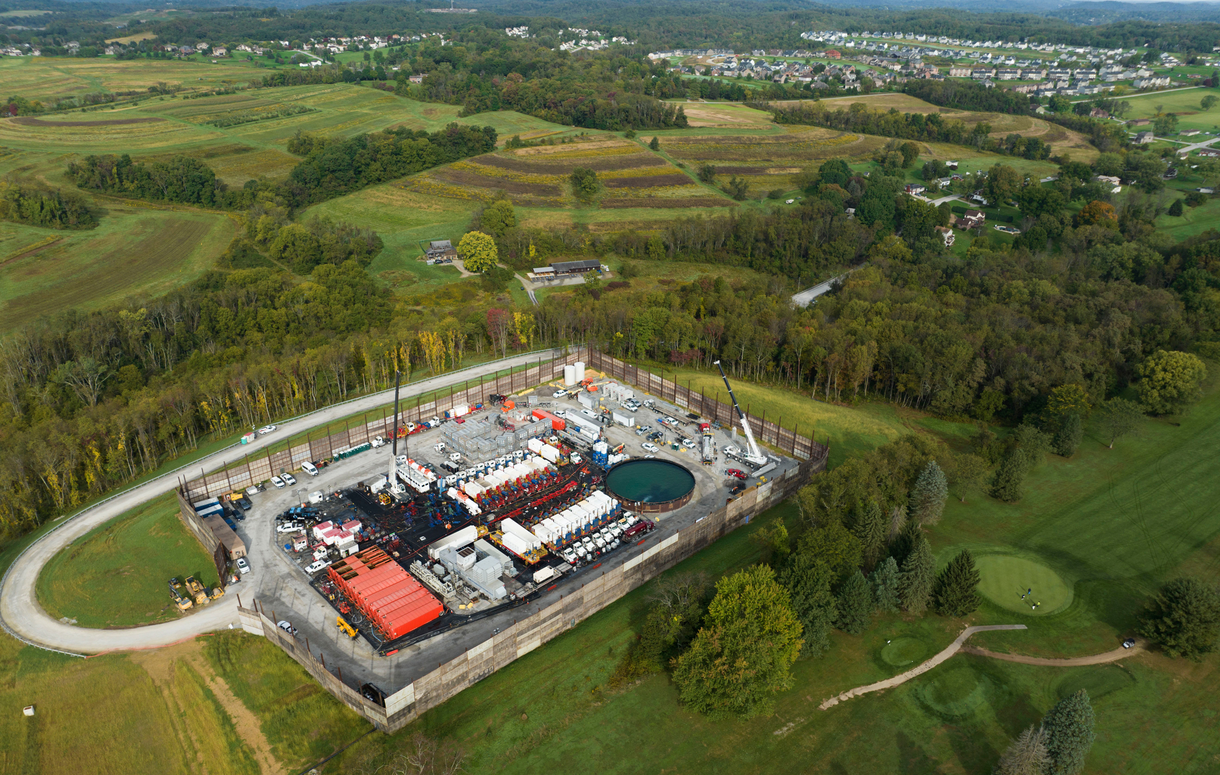 The image shows an industrial-looking pad surrounded by greenery, near homes