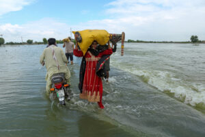 People carry their belongings through a flooded area after heavy monsoon rainfall in Punjab, Pakistan on Aug. 25, 2022. Credit: Shahid Saeed Mirza/AFP via Getty Images