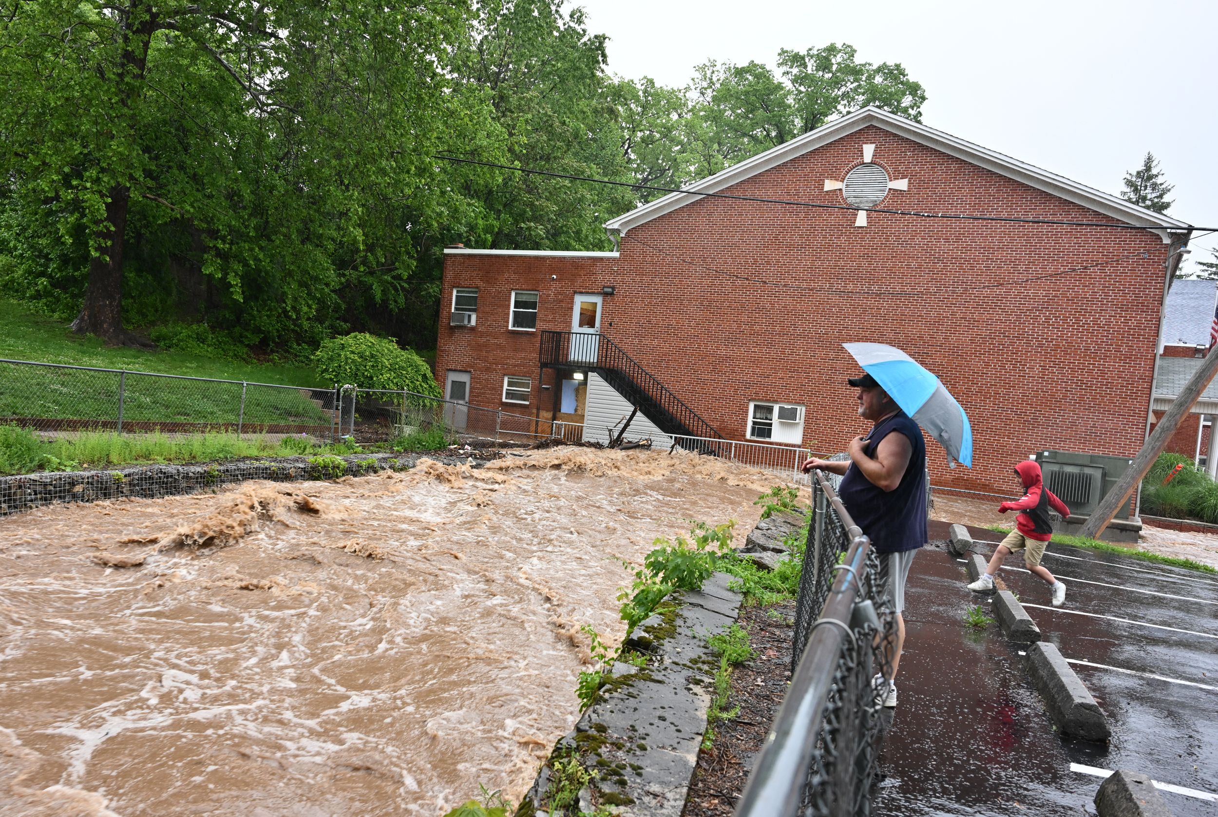 Chaz Netzer and his son Jaxson, 8, watch the deluge of water gathering up at the Calvary Christian Academy as flash flood warnings are in effect on May 13 in Cresaptown, M.D. Credit: Ricky Carioti/The Washington Post via Getty Images