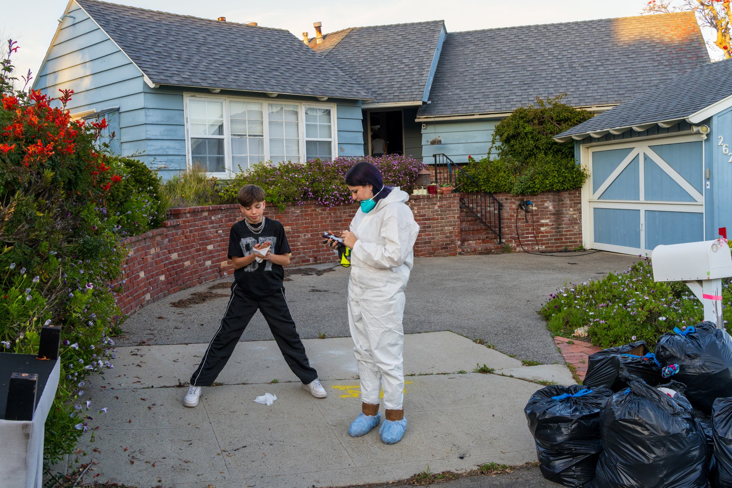 Leaf cleans his hands after stripping off his PPE following a long day of sorting through his belongings, as his sister, River, reads off dinner options from her phone.