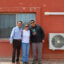 Red Feather staff (from left) Duane Tsinigine, Tavanne Sousa and Tyler Puente stand next to a heat pump installed with the nonprofit’s help at a home on the Hopi Reservation. Credit: Wyatt Myskow/Inside Climate News