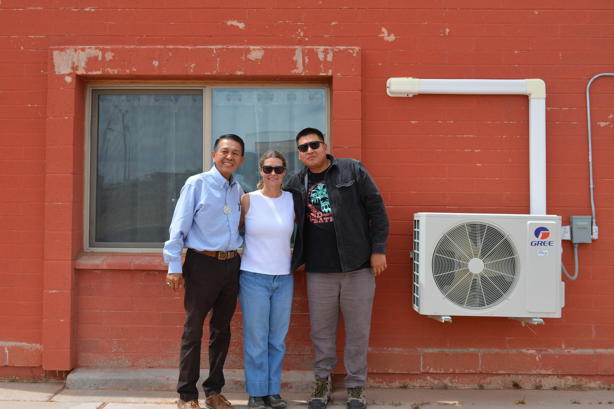 Red Feather staff (from left) Duane Tsinigine, Tavanne Sousa and Tyler Puente stand next to a heat pump installed with the nonprofit’s help at a home on the Hopi Reservation. Credit: Wyatt Myskow/Inside Climate News