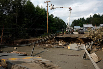 Utility workers attempt to clear wires on July 30, 2024, before contractors can repair a collapsed bridge after flash floods hit the area in St. Johnsbury, Vt. Credit: Danielle Parhizkaran/The Boston Globe via Getty Images