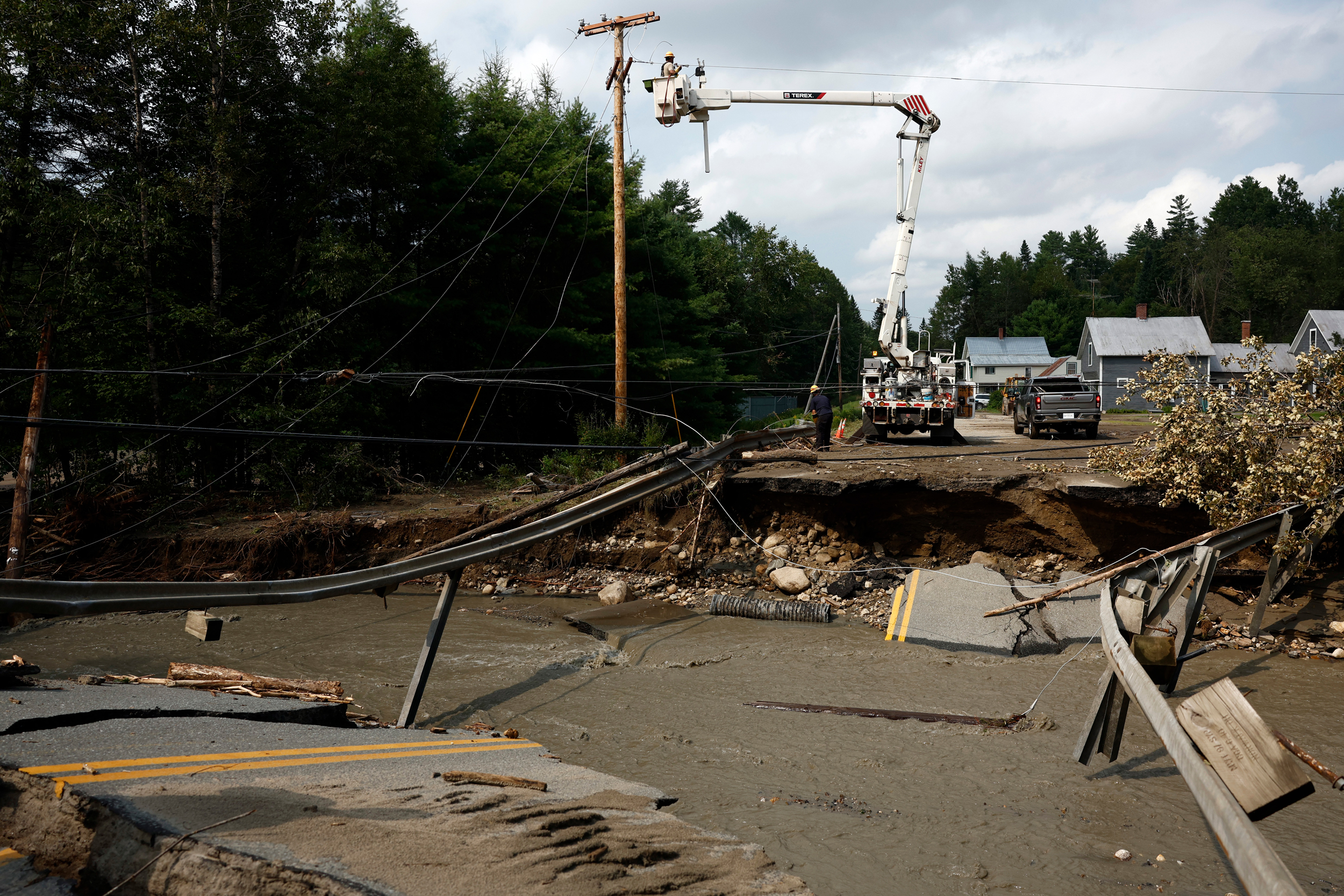 Utility workers attempt to clear wires on July 30, 2024, before contractors can repair a collapsed bridge after flash floods hit the area in St. Johnsbury, Vt. Credit: Danielle Parhizkaran/The Boston Globe via Getty Images