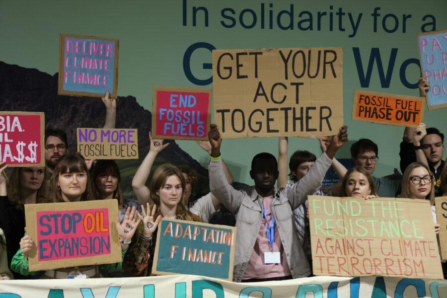 People, many of them young, hold signs with messages like "Get Your Act Together," "Deliver Climate Finance" and "End Fossil Fuels."