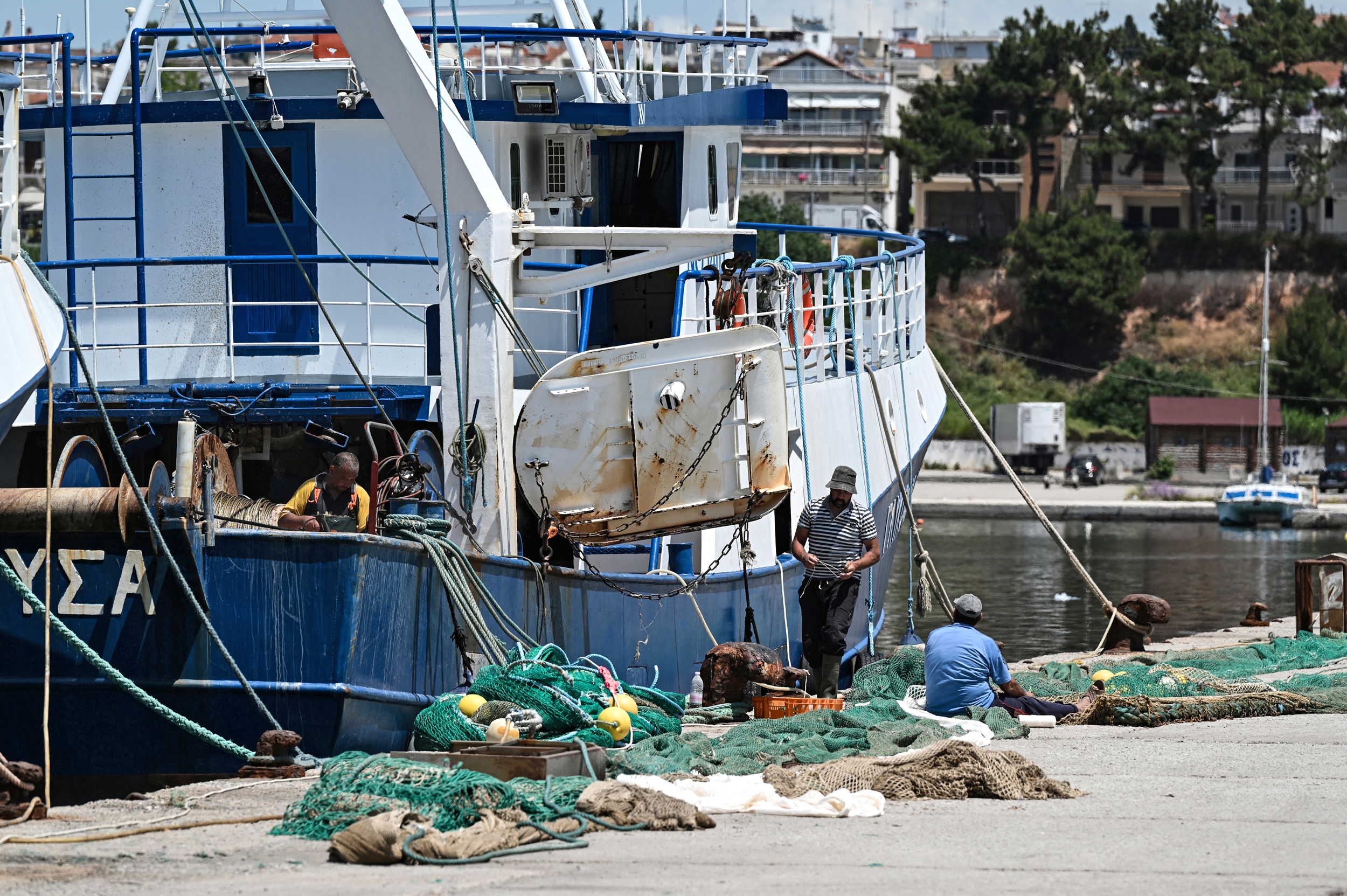 Workers handle a fishing net next to a commercial trawler docked at the port of Nea Michaniona in northern Greece on May 22. Credit: Sakis Mitrolidis/AFP via Getty Images