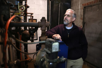Rev. Nathan Ives of the St. Peter’s-San Pedro Episcopal Church in Salem, Mass., stands next to an aging gas-fired, steam boiler in the church basement. Credit: Jonathan Wiggs/Boston Globe