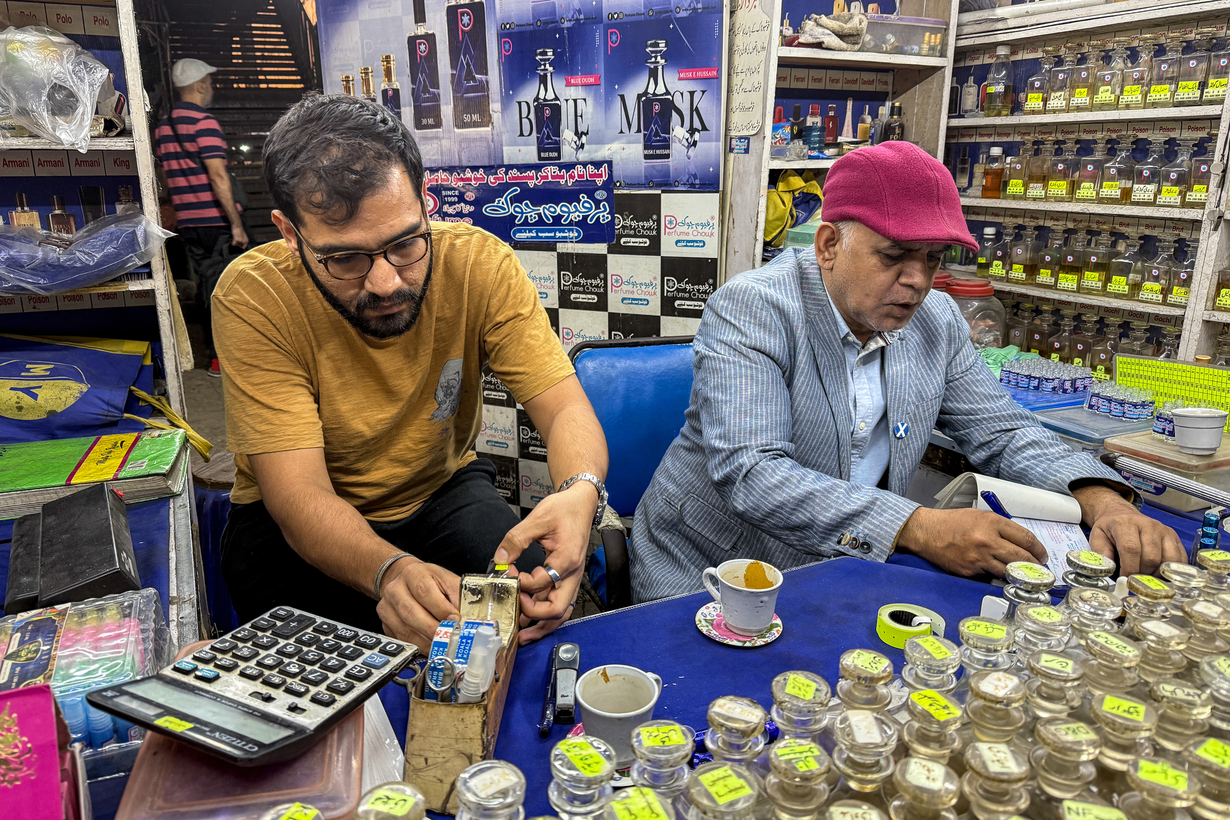Ali Zaid (left) readies a perfume bottle for a customer, while shop owner Mursaleen Sherwani writes out a receipt in Karachi. Credit: Aman Azhar/Inside Climate News