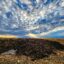 In the image, the sky is dramatically blue with interesting clouds above the manure and fields