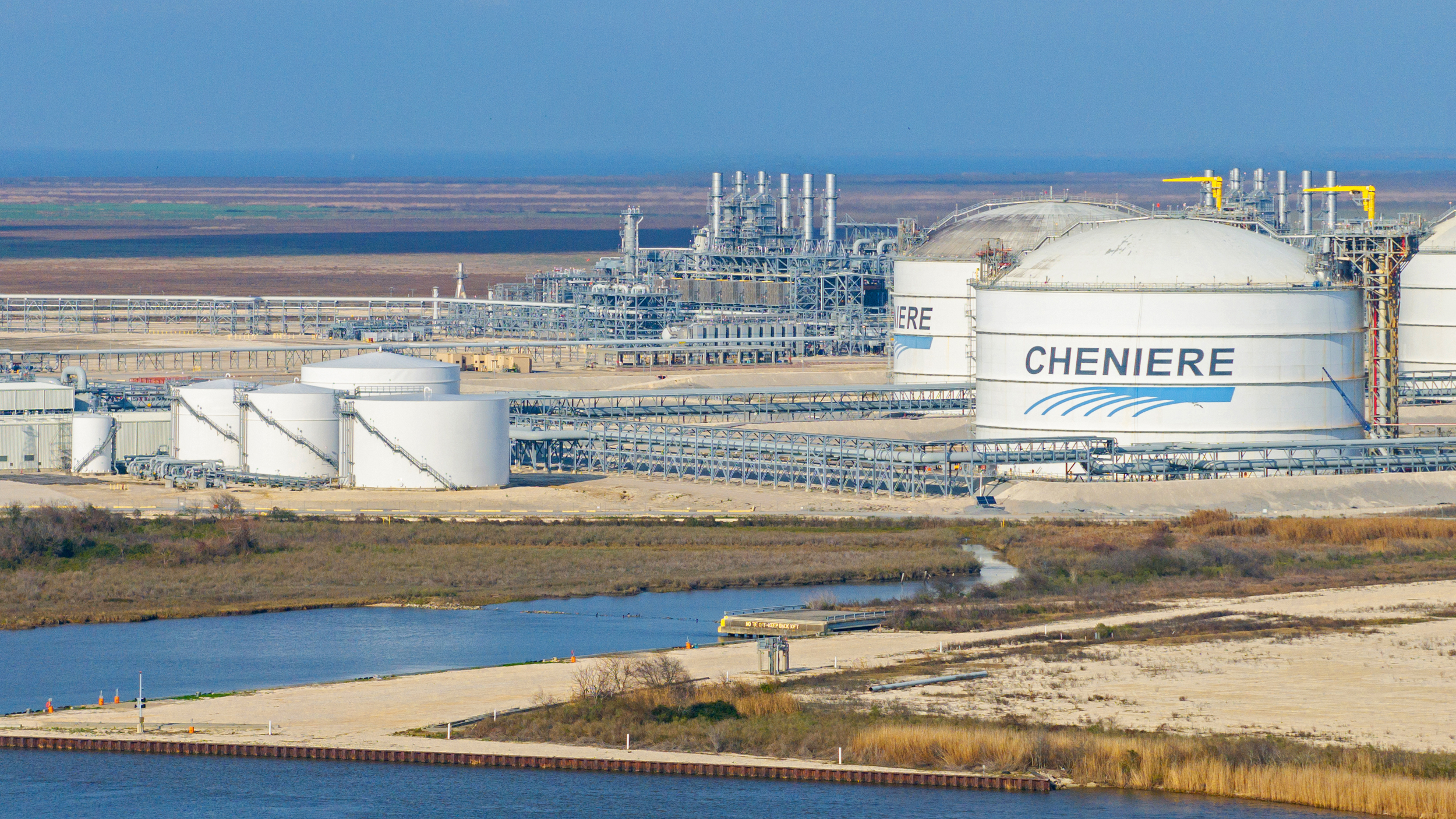 An aerial view of a Cheniere Energy liquefied natural gas plant, showing white storage tanks with the company's logo