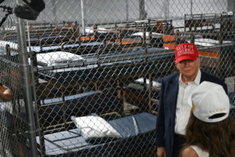 President Donald Trump speaks with Homeland Security Secretary Kristi Noem as they tour a migrant detention center, dubbed “Alligator Alcatraz,” located within Florida’s Big Cypress National Preserve. Credit: Andrew Caballero-Reynolds/AFP via Getty Images