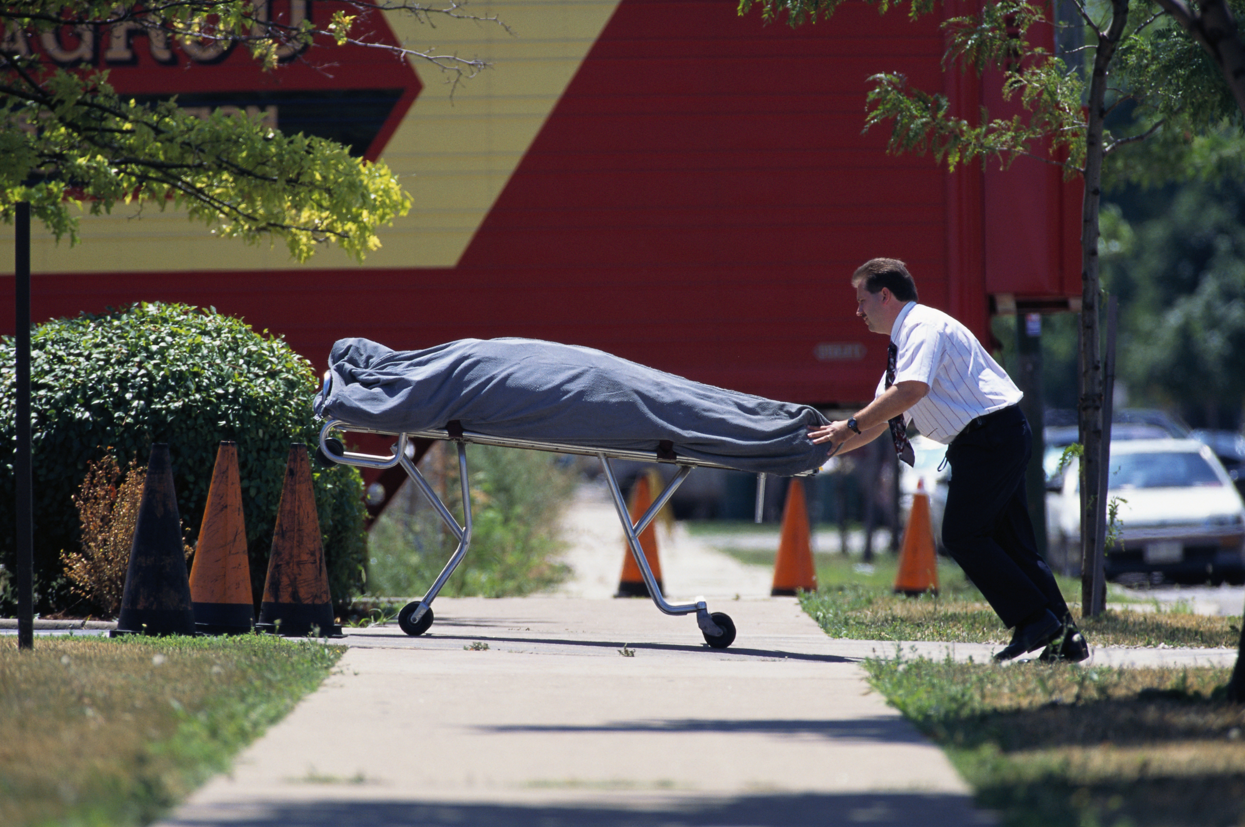 A man pushes a gurney covered with a body bag along a sidewalk