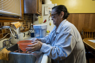She is filling an orange bowl with water from her sink, which has a filter attached. Beside the sink is a filtered water pitcher.