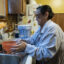 She is filling an orange bowl with water from her sink, which has a filter attached. Beside the sink is a filtered water pitcher.