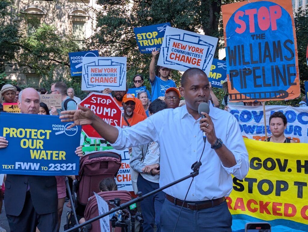 New York Lt. Gov. Antonio Delgado is speaking into a microphone, surrounded by people holding signs