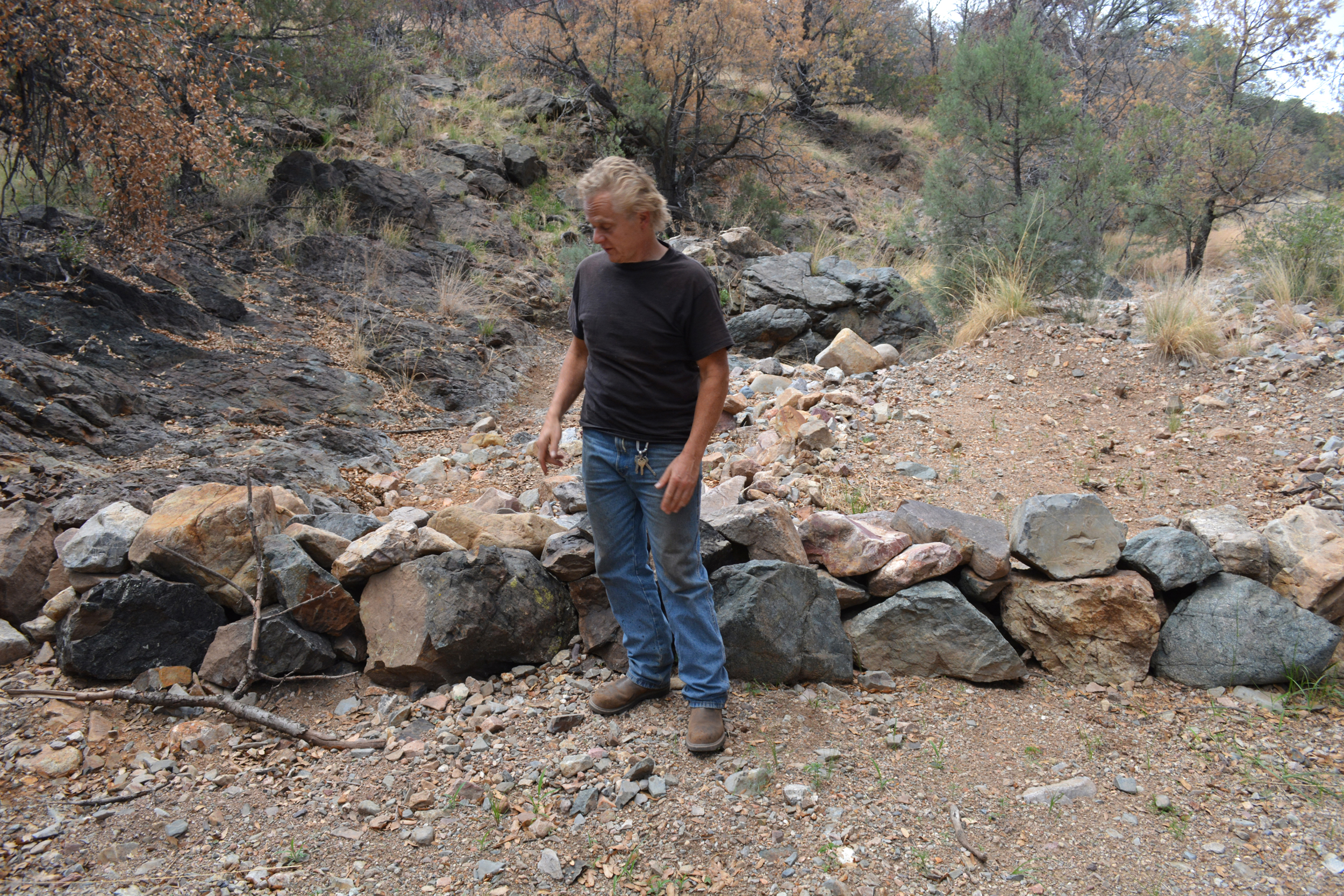 John Nordstrom stands before a rock dam he built on his property in Patagonia, Ariz., on July 9. Rock dams slows the speed of water, allowing it to better recharge the aquifer underground. Credit: Wyatt Myskow/Inside Climate News