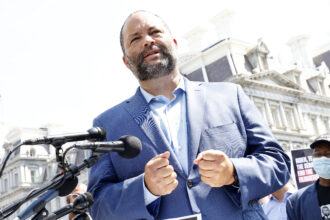 Ben Jealous, pictured in a blue dress shirt and blue blazer, is beside microphones outdoors