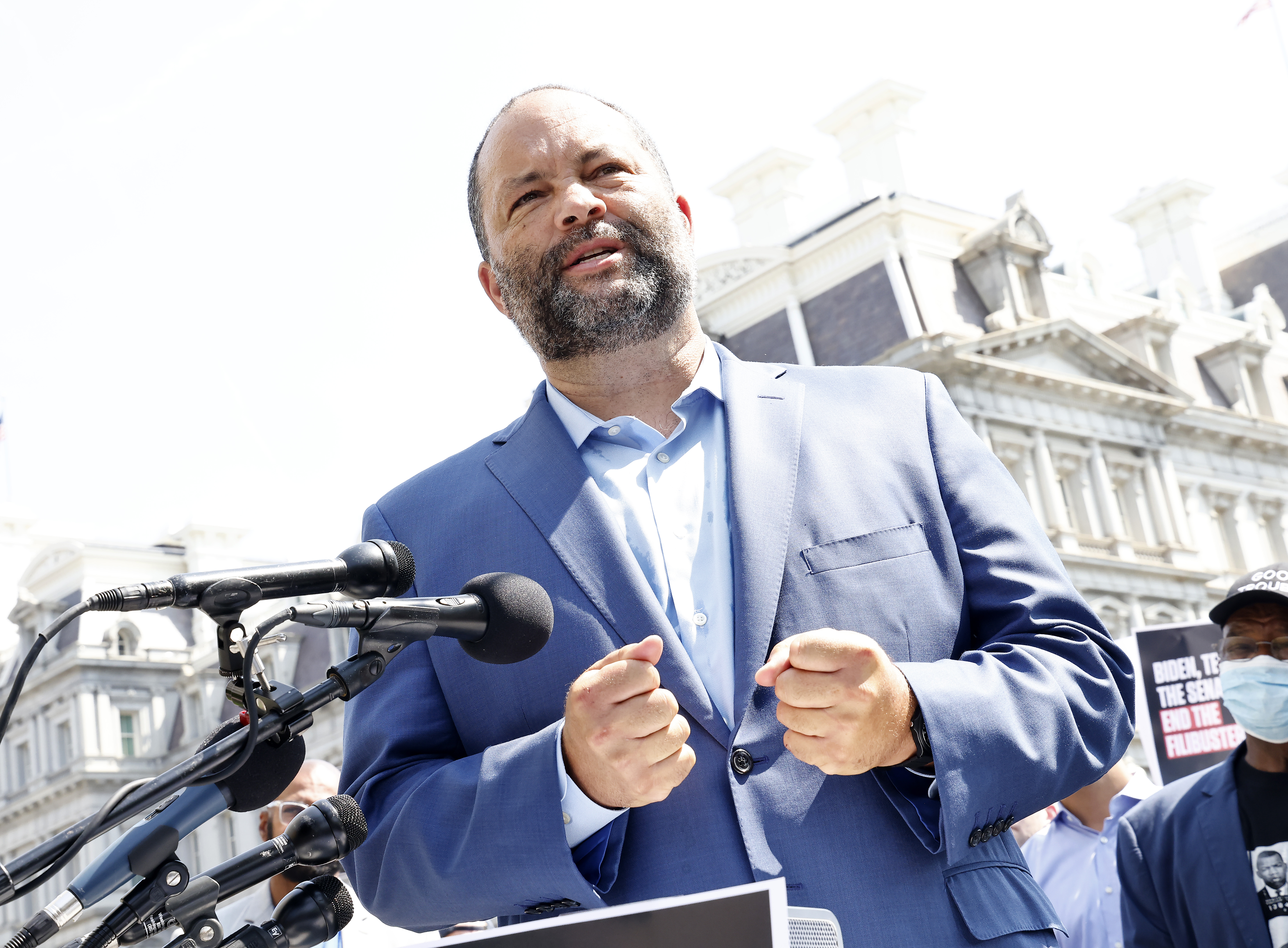 Ben Jealous, pictured in a blue dress shirt and blue blazer, is beside microphones outdoors