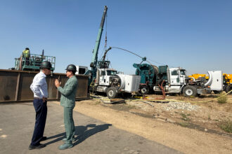 Bedrock Energy CTO Silviu Livescu (right) and Sen. John Hickenlooper (D-Colo.) talk in front of a drill rig on Wednesday at the Northwest Colorado Business District in Hayden, Colo. Credit: Emily Goldfield