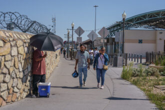 A vendor sells bottled water while shading himself with an umbrella at the exit of the Paso del Norte International Bridge during triple-digit temperatures in El Paso on Aug. 7.