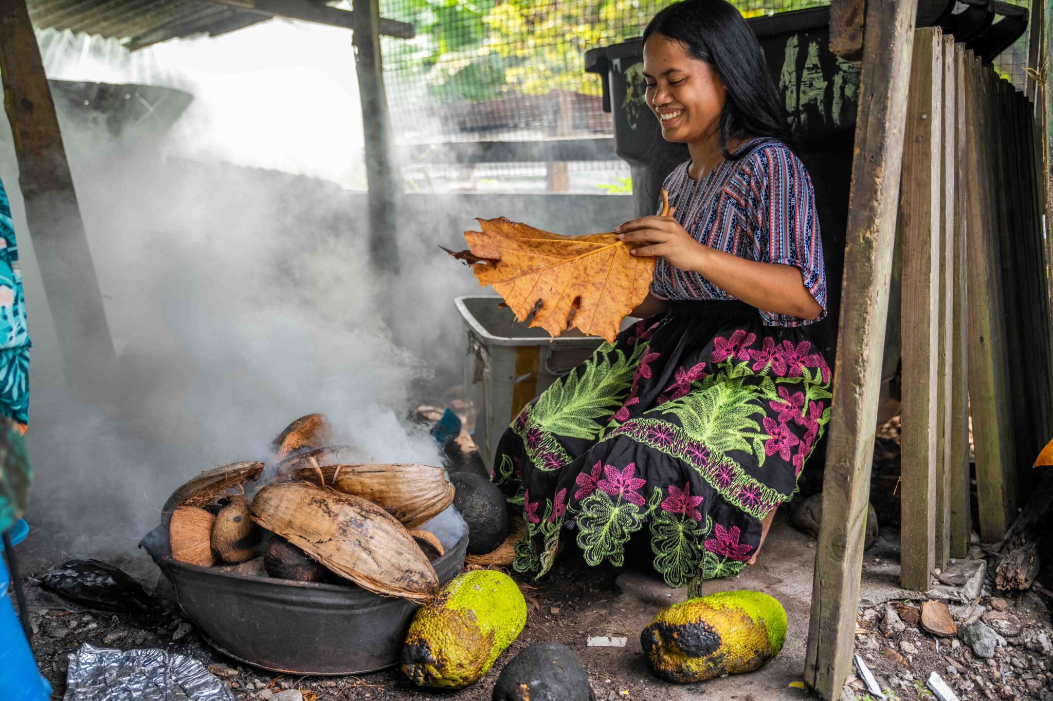 Hemne Naisher tends to a fire for roasting breadfruit, fanning it with the tree’s leaves. Credit: Chewy Lin/Civil Beat