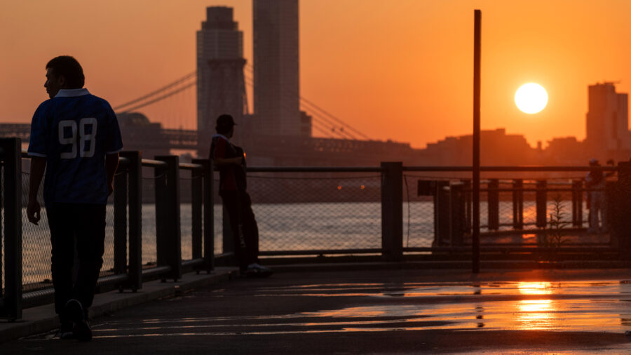 People walk along the East River in Brooklyn at sunrise on Aug. 12, as New York City experiences an air quality health advisory. Credit: Spencer Platt/Getty Images