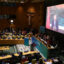 Xi Jinping is visible on a large screen; in the room, dozens of people are seated