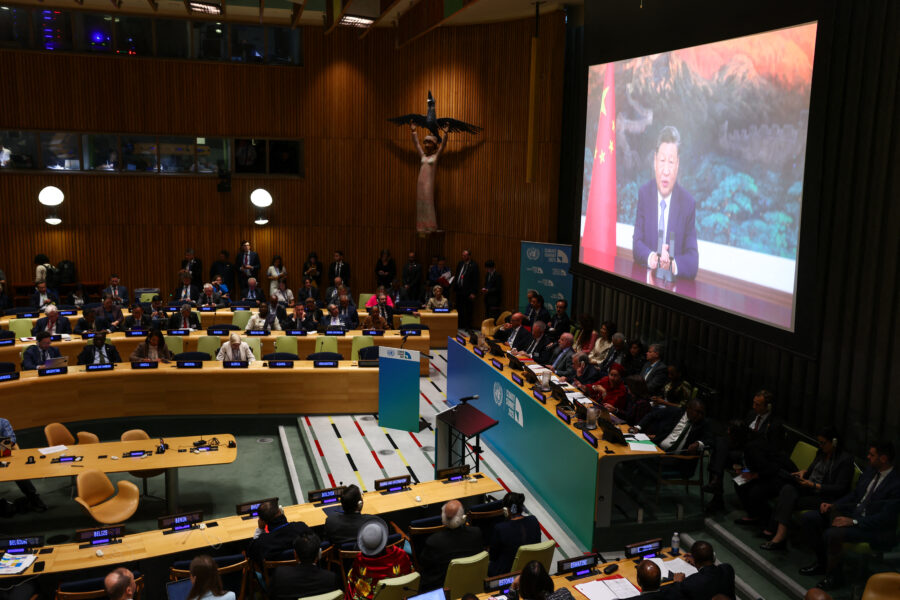 Xi Jinping is visible on a large screen; in the room, dozens of people are seated