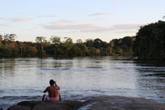 A Wayana Indigenous man sits on the embankment of the Maroni River in Southern French Guiana. Credit: Benoit Virginie