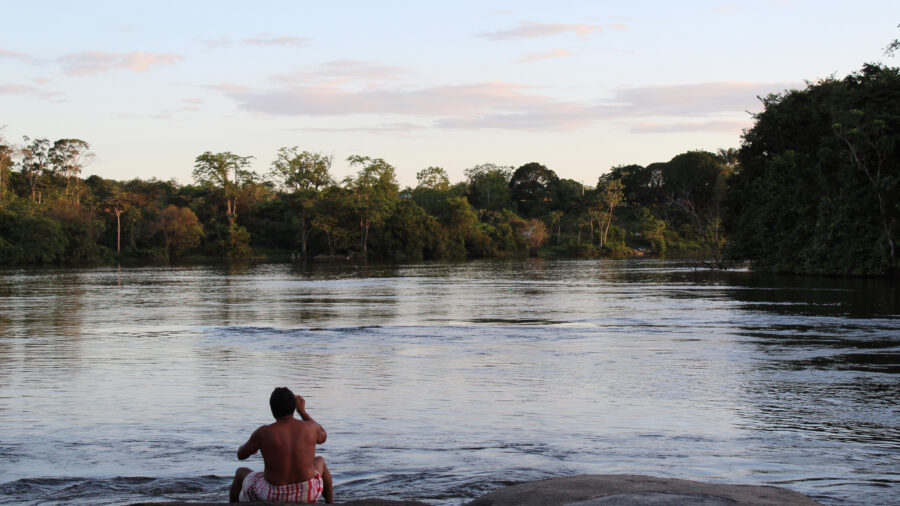 A Wayana Indigenous man sits on the embankment of the Maroni River in Southern French Guiana. Credit: Benoit Virginie