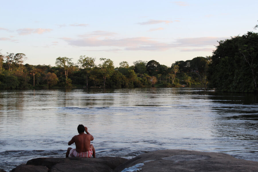 A Wayana Indigenous man sits on the embankment of the Maroni River in Southern French Guiana. Credit: Benoit Virginie