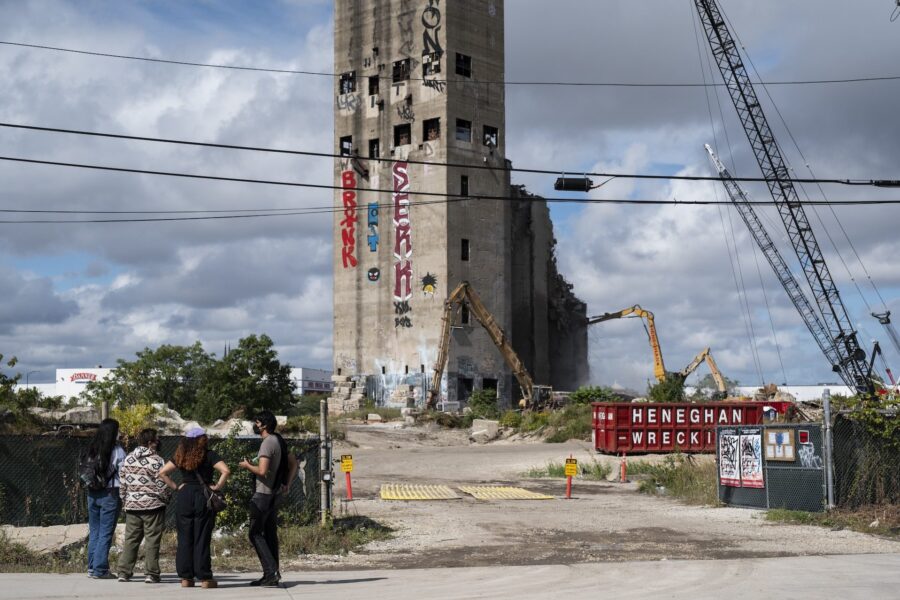 The organizers are standing in a cluster in the foreground. Beyond them are the silos, tagged with graffiti, and demolition equipment.