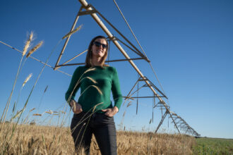 Sarah Jones stands under a center pivot irrigation unit, with a few stems of rye in the foreground, on her farm in Colorado’s San Luis Valley. Credit: Hart Van Denburg/CPR News