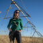 Sarah Jones stands under a center pivot irrigation unit, with a few stems of rye in the foreground, on her farm in Colorado’s San Luis Valley. Credit: Hart Van Denburg/CPR News