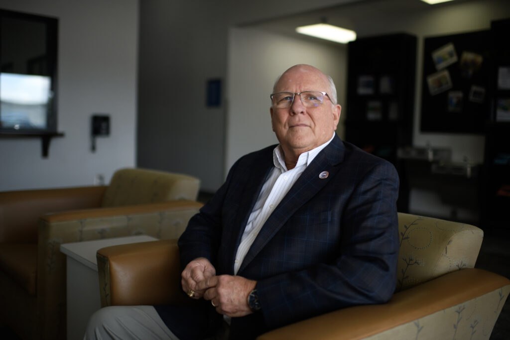 Tom Ramsey is sitting in a chair, looking at the camera with a serious expression