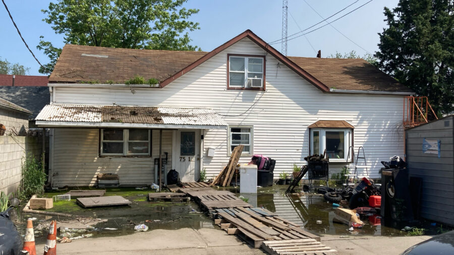 Water pools in the front yard of a house in “The Hole” of New York City. A makeshift bridge has been constructed out of wooden planks. Credit: Lauren Dalban/Inside Climate News