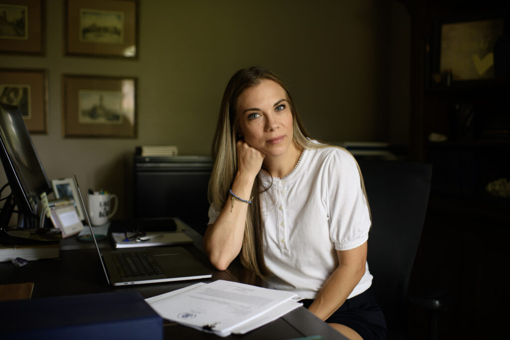 Jackie Medcalf is sitting at a desk by a computer, pictures on the wall behind her